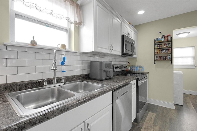 kitchen with white cabinets, dark countertops, dark wood-style flooring, stainless steel appliances, and a sink