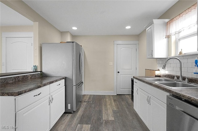 kitchen featuring white cabinets, dark countertops, appliances with stainless steel finishes, dark wood-style flooring, and a sink