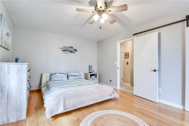 bedroom featuring baseboards, a barn door, a ceiling fan, and light wood-style floors