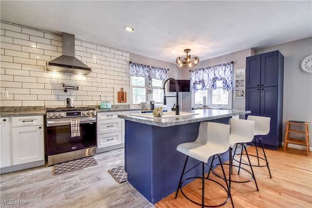 kitchen featuring a breakfast bar area, light wood finished floors, tasteful backsplash, stainless steel gas range oven, and wall chimney exhaust hood