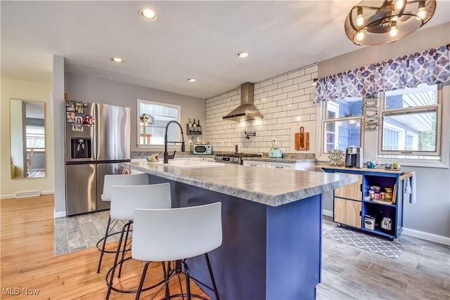 kitchen featuring visible vents, light wood-style floors, appliances with stainless steel finishes, wall chimney range hood, and a sink