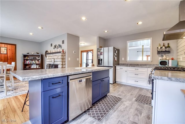 kitchen with stainless steel appliances, a sink, blue cabinetry, and wall chimney exhaust hood