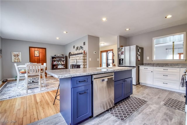 kitchen with blue cabinets, stainless steel appliances, light countertops, white cabinetry, and a sink