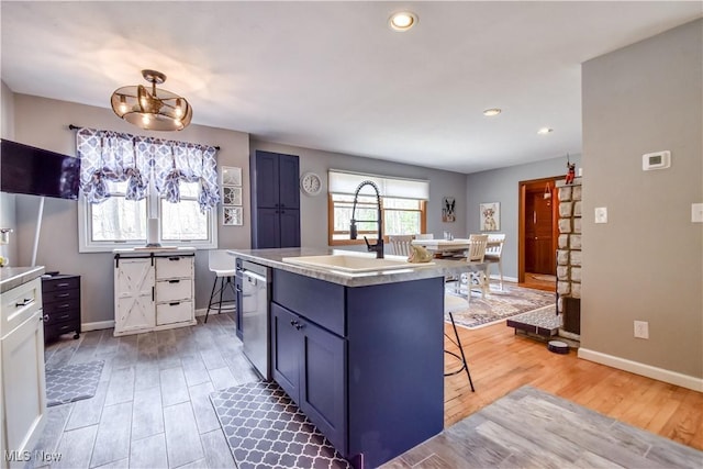 kitchen with light wood finished floors, light countertops, a sink, dishwasher, and a kitchen breakfast bar