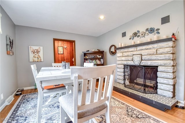 dining area with visible vents, a stone fireplace, baseboards, and wood finished floors