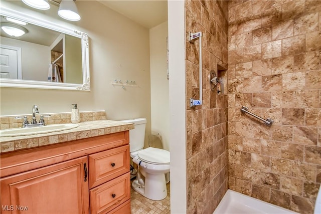 bathroom with toilet, tiled shower, and vanity