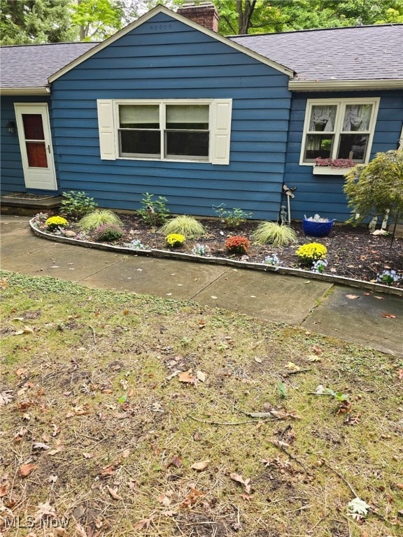 view of side of property with roof with shingles and a chimney