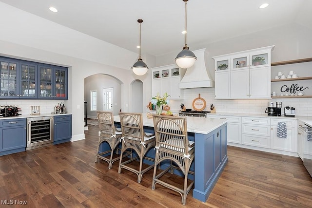 kitchen with arched walkways, blue cabinetry, custom range hood, dark wood-type flooring, and beverage cooler