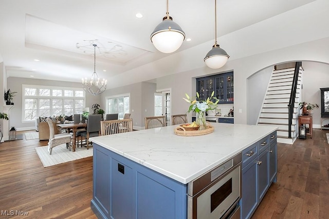 kitchen featuring a tray ceiling, dark wood-style flooring, a kitchen island, and blue cabinetry