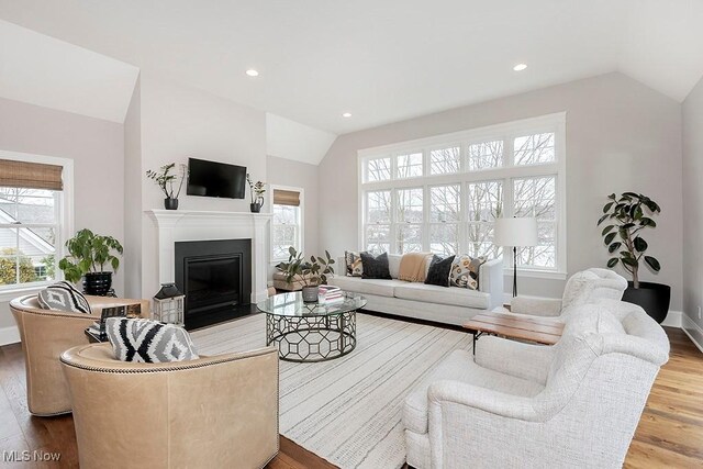 living area with recessed lighting, a glass covered fireplace, vaulted ceiling, wood finished floors, and baseboards