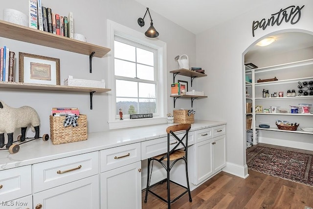 home office with dark wood-style floors and arched walkways