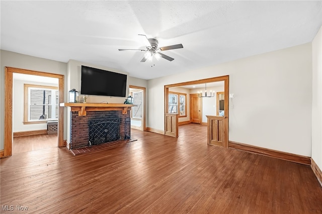 unfurnished living room featuring a fireplace, baseboards, wood finished floors, and ceiling fan with notable chandelier