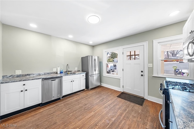 kitchen featuring wood finished floors, appliances with stainless steel finishes, a sink, and white cabinets