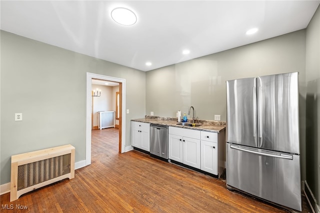 kitchen with stainless steel appliances, radiator, white cabinets, a sink, and wood finished floors