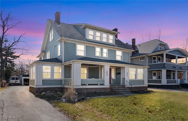 traditional style home with roof with shingles, a porch, a lawn, and a chimney