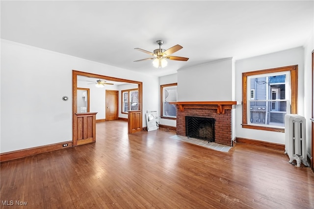 unfurnished living room with baseboards, a ceiling fan, radiator heating unit, dark wood-style flooring, and a brick fireplace