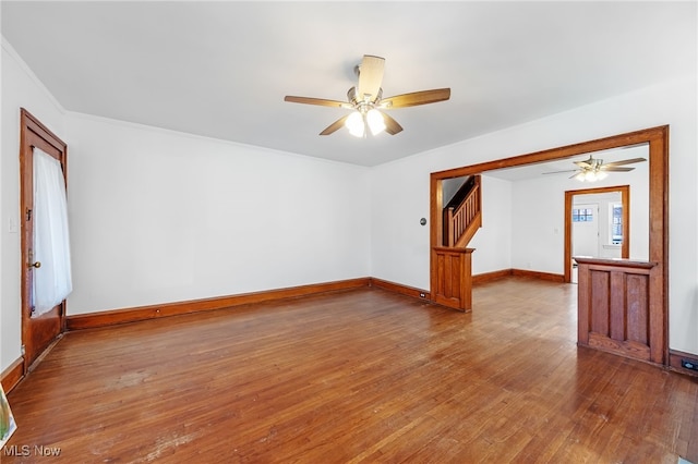 unfurnished room featuring wood-type flooring, ceiling fan, baseboards, and stairs