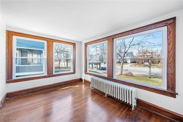 spare room with baseboards, plenty of natural light, radiator heating unit, and wood finished floors