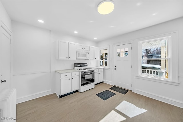 kitchen featuring white appliances, white cabinets, light countertops, light wood-type flooring, and recessed lighting