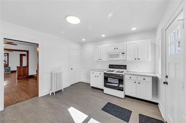 kitchen with radiator, white microwave, light countertops, white cabinetry, and gas stove