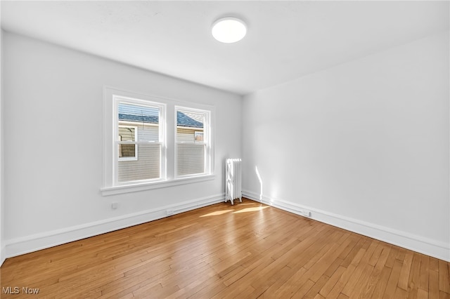 empty room featuring radiator, wood-type flooring, and baseboards