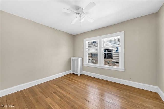 spare room featuring light wood-type flooring, a ceiling fan, and baseboards