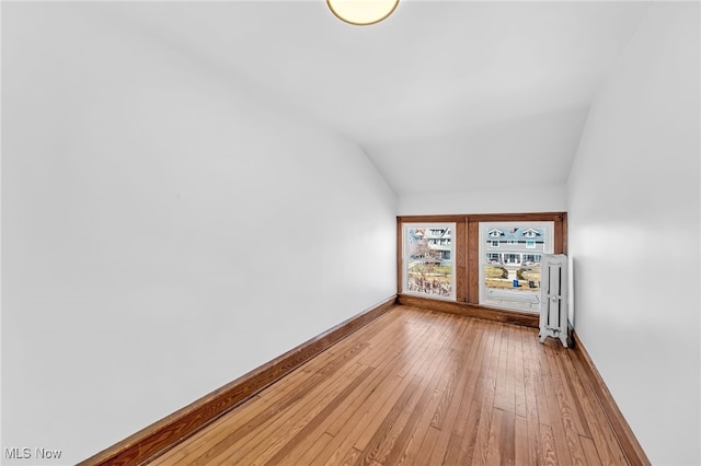 spare room featuring vaulted ceiling, hardwood / wood-style flooring, and baseboards