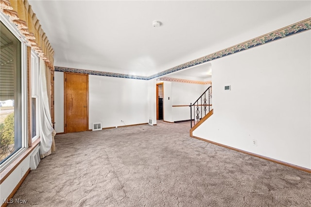 carpeted spare room featuring visible vents, stairway, and baseboards