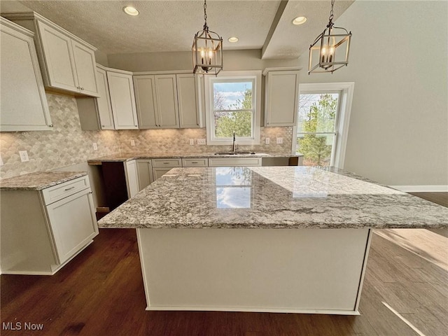 kitchen with light stone countertops, decorative backsplash, dark wood finished floors, and a center island