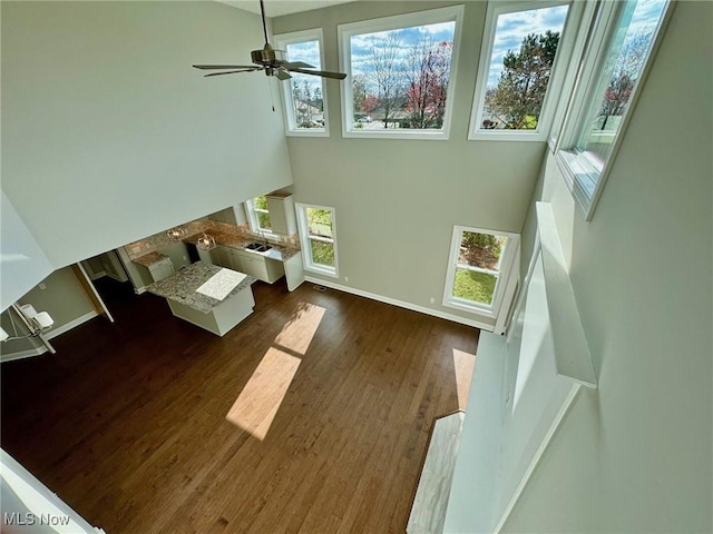 unfurnished living room featuring a towering ceiling, a ceiling fan, baseboards, and wood finished floors