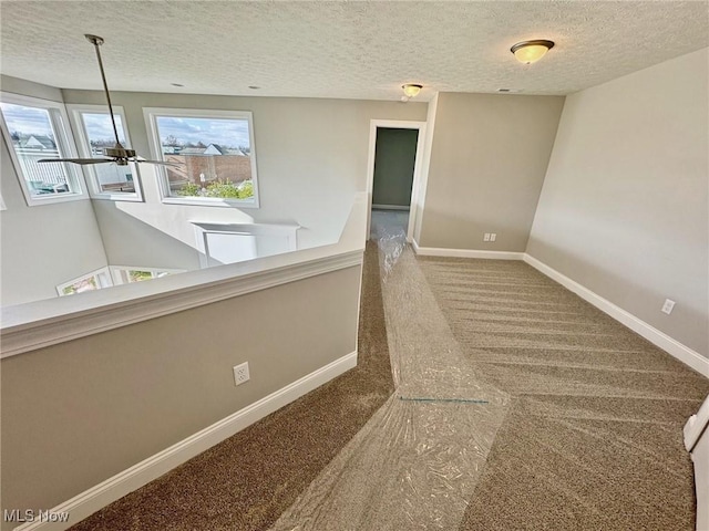 hall with carpet, a textured ceiling, and baseboards