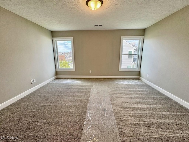 unfurnished room featuring a textured ceiling, carpet floors, visible vents, and baseboards