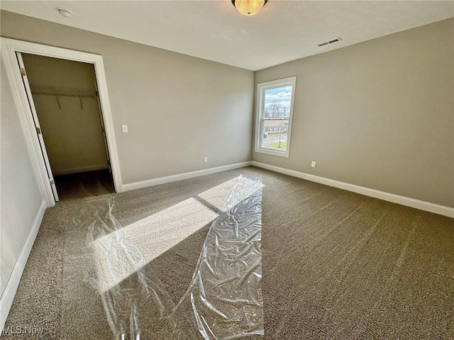 unfurnished bedroom with carpet floors, visible vents, baseboards, a closet, and a walk in closet