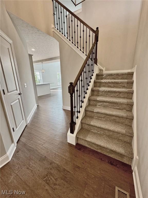 stairway featuring baseboards, a high ceiling, visible vents, and wood finished floors