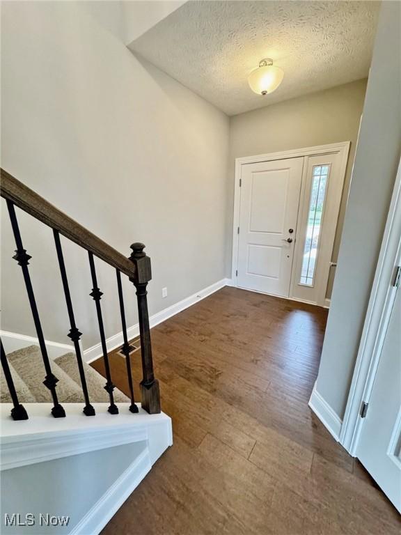 entryway with dark wood-style floors, stairway, a textured ceiling, and baseboards