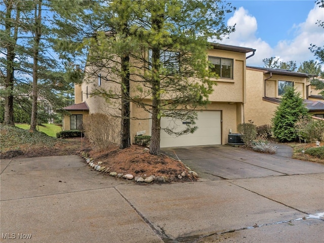 view of side of property with central air condition unit, stucco siding, driveway, and a garage