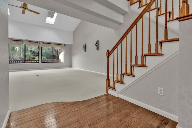 unfurnished living room with a ceiling fan, wood finished floors, a skylight, baseboards, and stairs