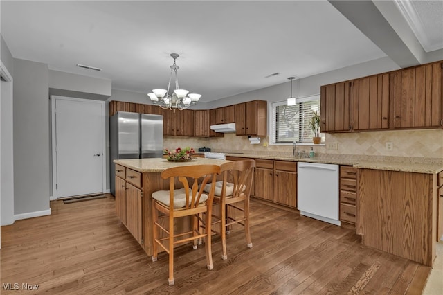 kitchen with visible vents, under cabinet range hood, a kitchen island, white dishwasher, and light wood finished floors