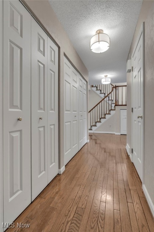 corridor with stairway, wood-type flooring, a textured ceiling, and baseboards