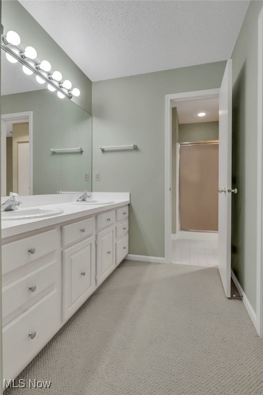 bathroom with double vanity, a shower, a textured ceiling, and a sink