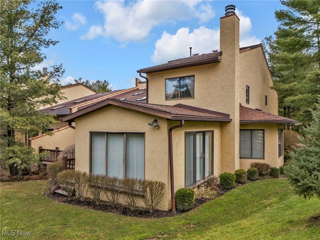 back of property with stucco siding, a chimney, a lawn, and a shingled roof