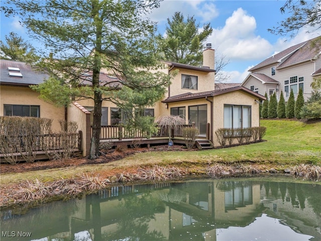 back of house featuring a wooden deck, a lawn, a chimney, and stucco siding