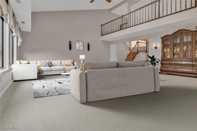 carpeted living area featuring visible vents, baseboards, ceiling fan, stairway, and a high ceiling