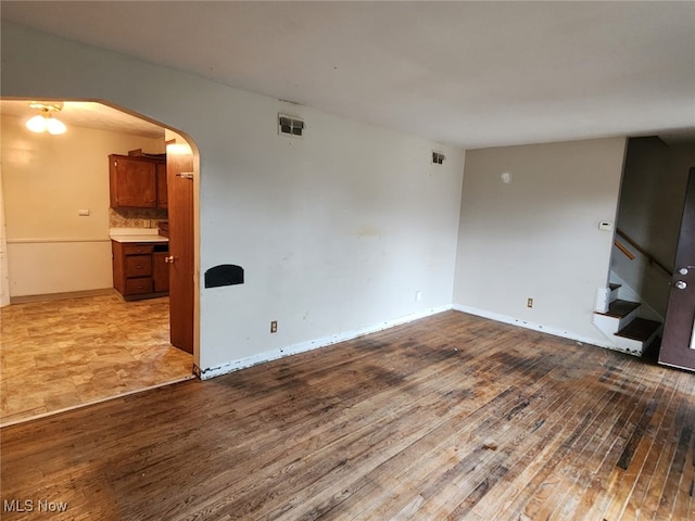 unfurnished living room featuring arched walkways, wood finished floors, stairs, and baseboards