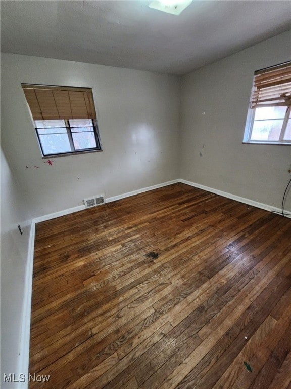 empty room featuring baseboards, visible vents, and dark wood-style flooring