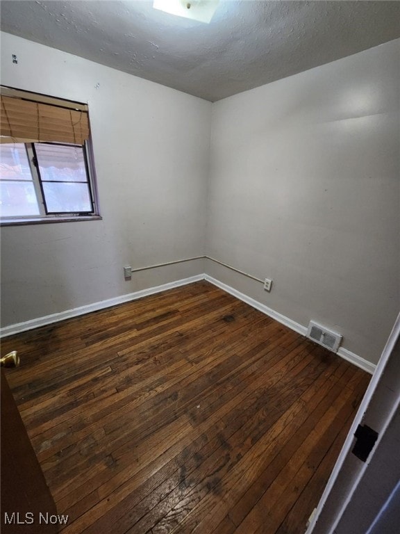 spare room featuring dark wood-style floors, visible vents, a textured ceiling, and baseboards