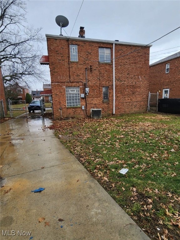 view of side of property featuring a gate, brick siding, fence, and central AC unit