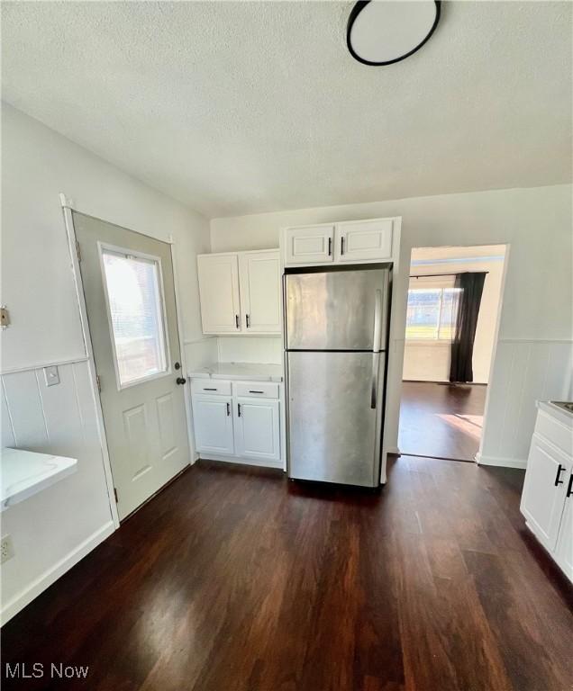 kitchen featuring dark wood-style flooring, freestanding refrigerator, white cabinets, wainscoting, and a textured ceiling