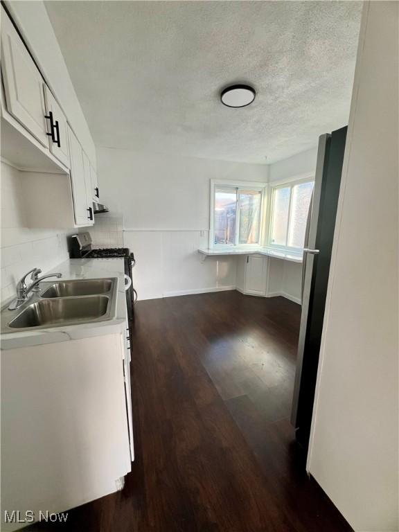 kitchen with white cabinets, dark wood finished floors, light countertops, a textured ceiling, and a sink