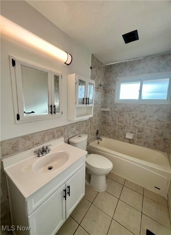 bathroom featuring tile walls, shower / bathtub combination, toilet, a textured ceiling, and tile patterned flooring